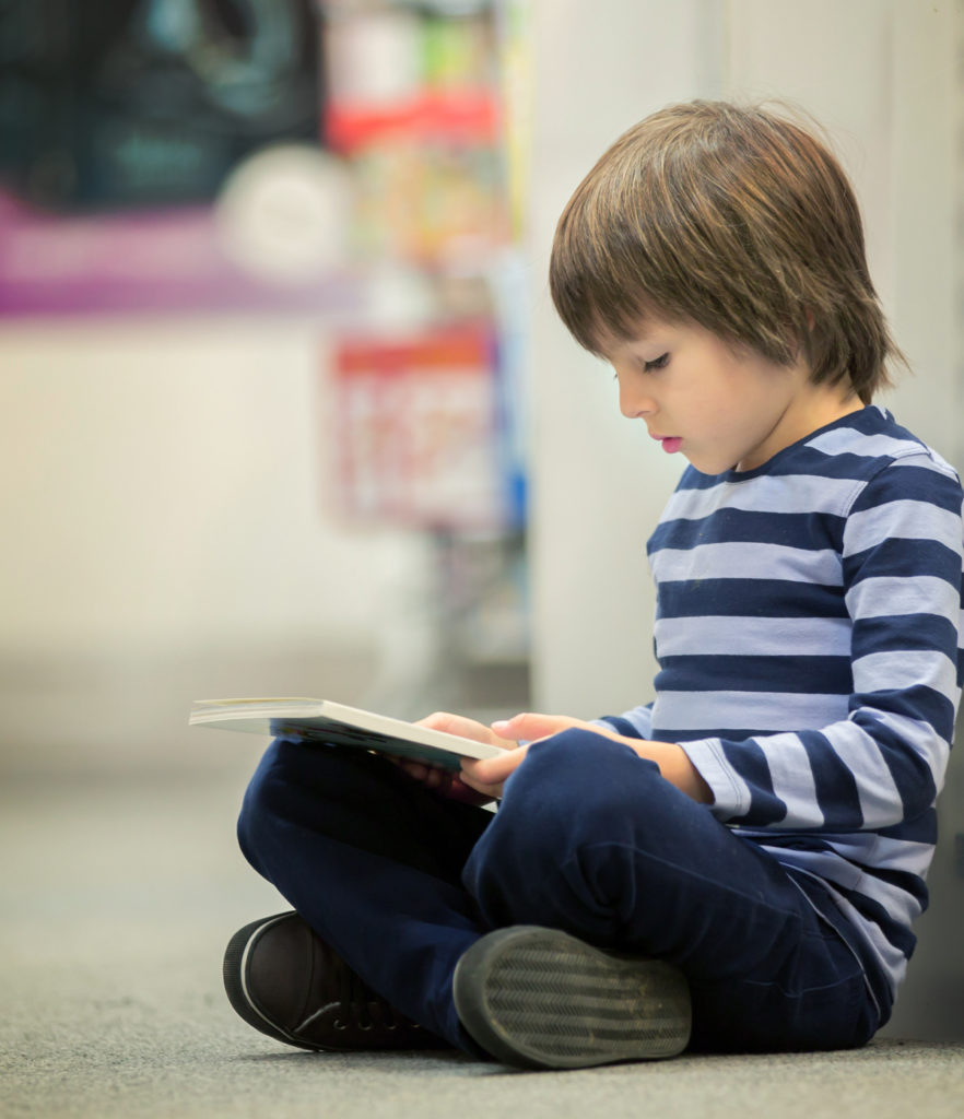 Adorable little child, boy, sitting in a book store, reading books